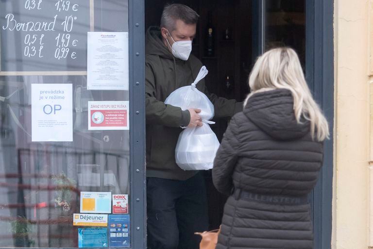Un hombre con mascarilla para protegerse del coronavirus recibe comida para llevar en Bratislava, Eslovaquia, el 25 de noviembre del 2021.  (Martin Baumann/TASR via AP)