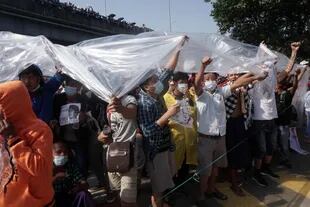 La gente se cubre con plástico por los cañones de agua durante una manifestación contra el golpe militar en Rangún