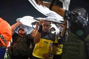 El árbitro Dario Herrera sale protegido por los escudos de la policía que lo reparan de los proyectiles arrojados desde la platea de Lanús