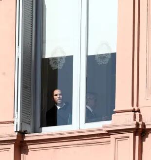 Martín Guzmán se asoma desde una ventana de la Casa Rosada, detrás está Alberto Fernández, antes del anuncio por el cambio en ganancias