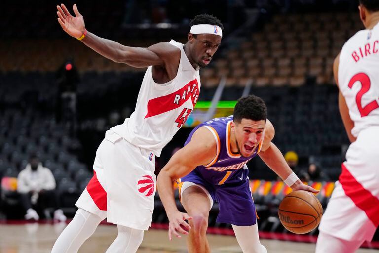 El base de los Suns de Phoenix Devin Booker pasa frente al alero de los Raptors de Toronto Pascal Siakam durante la primera mitad del partido de la NBA en Toronto, el martes 11 de enero de 2022. (Frank Gunn/The Canadian Press vía AP)