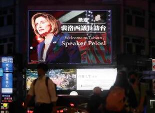 Numerosas personas pasan frente a una pantalla enorme en la que se da la bienvenida a la visita de la presidenta de la Cámara de Representantes de Estados Unidos, Nancy Pelosi, a Taipei, Taiwán, el martes 2 de agosto de 2022. (AP Foto/Chiang Ying-ying)