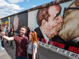 Una pareja se toma una selfie frente al beso de Brezhnev y Honecker, en el muro de Berlín; el autor del famoso grafiti murió hoy en la capital alemana