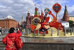Una voluntario salta para ser fotografiado por una compañero de equipo frente a un reloj que lleva la cuenta regresiva en la Plaza Roja en Moscú