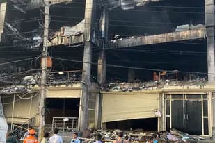 Personas alrededor de un edificio incendiado en Nueva Delhi el sábado 14 de mayo de 2022. La policía arrestó a dos dueños de una compañía que fabrica y produce cámaras de seguridad luego de que el fuego, al parecer desatado en su oficina en un edificio de cuatro pisos, mató a 27 personas e hirió a otras 12, dijeron las autoridades.  (AP Foto/Shonal Ganguly)