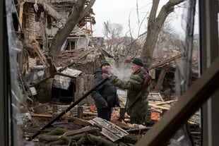 Andrey Goncharuk, de 68 años, a la derecha, miembro de la defensa territorial habla con un hombre en el patio de una casa dañada por un ataque aéreo ruso, según lugareños, en Gorenka, en las afueras de la capital, Kiev, Ucrania, el miércoles 2 de marzo de 2022