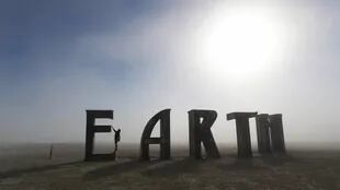Anita Vranckx, de Bélgica, cuelga de la E de una escultura que dice "Tierra" en el Burning Man en una mañana de polvo