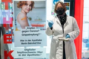 Sandra Fundel, farmacéutica de la farmacia Bahnhof Zoo, está parada afuera de la farmacia junto a un anuncio de vacunación en Berlín, Alemania, el lunes 7 de febrero de 2022. (Christophe Gateau/dpa vía AP)