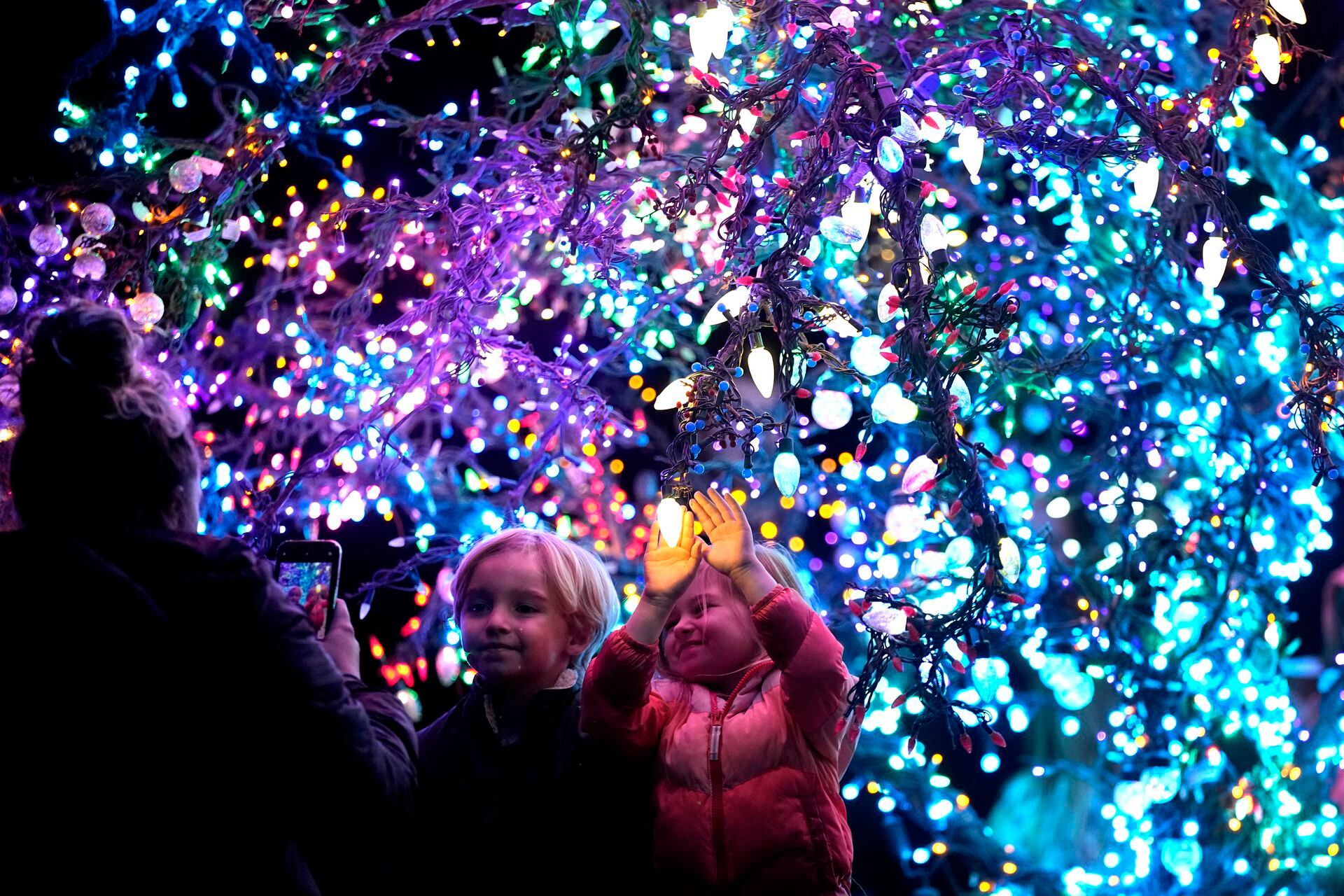 Los niños posan para una foto frente al árbol mágico de Lee's Summit en Lee's Summit, Missouri. El árbol solitario y modesto en un campo junto a una autopista está cubierto con más de 12,000 luces y atrae a miles de personas en cada temporada navideña