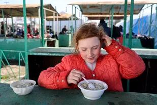 Una niña toma un plato de comida caliente distribuida por el Ministerio de Situaciones de Emergencia de la República Popular de Donetsk, en una zona controlada por las fuerzas separatistas prorrusas, en la localidad de Bezimenne, en el este de Ucrania, el 20 de abril de 2022. (AP Foto/Alexei Alexandrov)