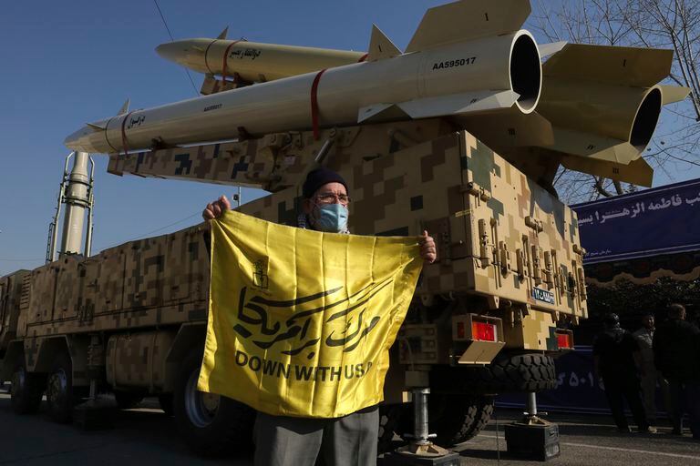 Un hombre muestra una pancarta con lemas contra Estados Unidos frente a los misiles Zolfaghar (arriba), Dezful (abajo) y Qiam (al fondo a la izquierda), durante una exhibición de las armas por parte de la Guardia Revolucionaria de Irán, el viernes 7 de enero de 2022, en Teherán, Irán. (AP Foto/Vahid Salemi)