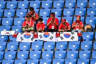 Los hinchas coreanos miran sus celulares mientras esperan a que empiece el partido