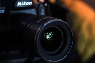 Los anillos olímpicos iluminados se reflejan en la lente de una cámara