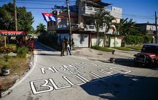 En esta foto de archivo tomada el 30 de enero de 2022, los residentes se paran junto a un cartel que dice "Abajo el bloqueo" en Santa Clara, provincia de Villa Clara, Cuba.