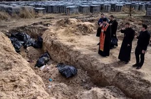 Priests pray in front of body bags at a mass grave on the grounds surrounding St. Andrew's Church in Bucha, on April 7, 2022, amid the Russian military invasion against Ukraine.  (Photo by Ronaldo Schmidt / AFP) / Ukraine - Russian conflict 100 days 100 photos
