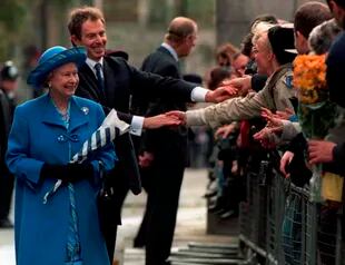 El primer ministro de Gran Bretaña, Tony Blair, sigue a la reina Isabel II mientras se encuentran con simpatizantes durante un paseo, luego de un servicio de acción de gracias en la Abadía de Westminster para celebrar el aniversario de bodas de oro de la reina y el príncipe Felipe, de pie al fondo, en Londres, en 1997