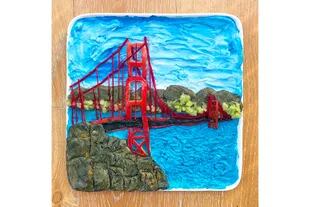 Emblemática postal del Golden Gate en San Francisco emplatado por Harley Langberg y hecho a base de yogurt mezclado con espirulina azul, manteca de maní mezclada con colorante negro para alimentos, manzana, kiwi y pasta teñida de rojo con colorante natural para alimentos.
