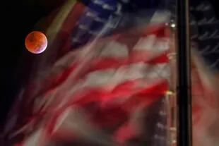 El eclipse lunar total es visto contra una bandera estadounidense al viento en el National Mall de Washington DC, Estados Unidos (AP Photo/J. David Ake)