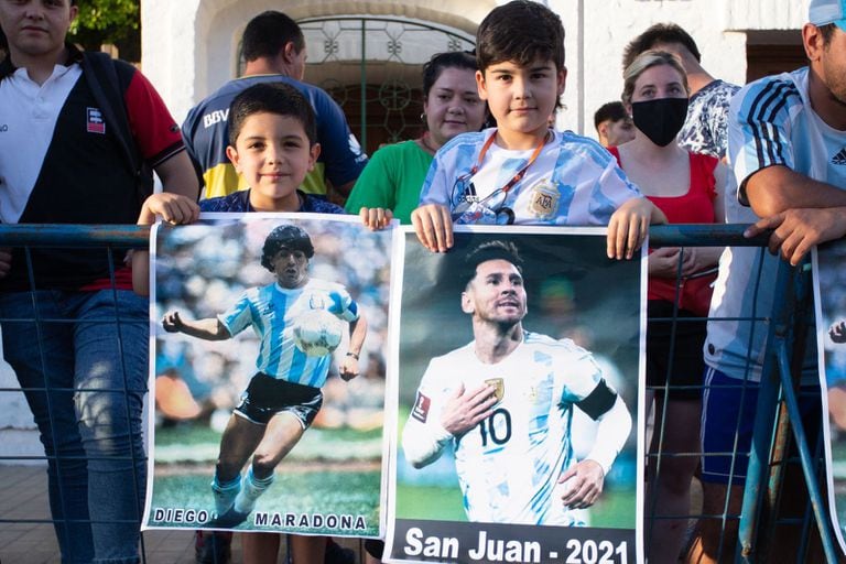 Dos chicos con carteles de Maradona y Messi en San Juan