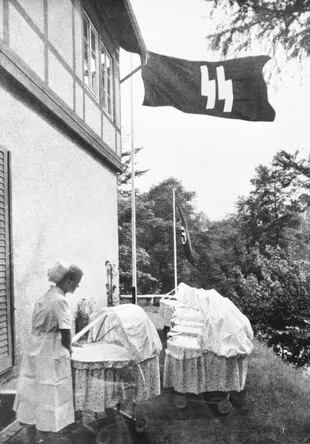 Una enfermera cuida a un bebé al aire libre mientras flamea una bandera con las runas SS