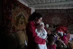 Anastasia Manha, de 23 años, mece a su hijo de dos meses, Mykyta, en el lugar donde vive con familiares tras supuestos bombardeos de fuerzas separatistas en Novognativka, en el este de Ucrania, el domingo 20 de febrero de 2022. (AP Foto/Evgeniy Maloletka)