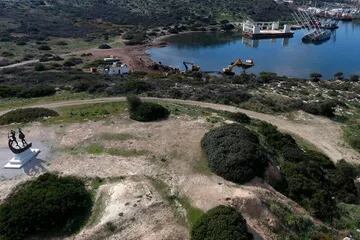 Maquinarias pesadas destruyen embarcaciones abandonadas, mientras el Monumento de la Batalla de Salamina se encuentra en lo alto de una colina en la isla homónima
