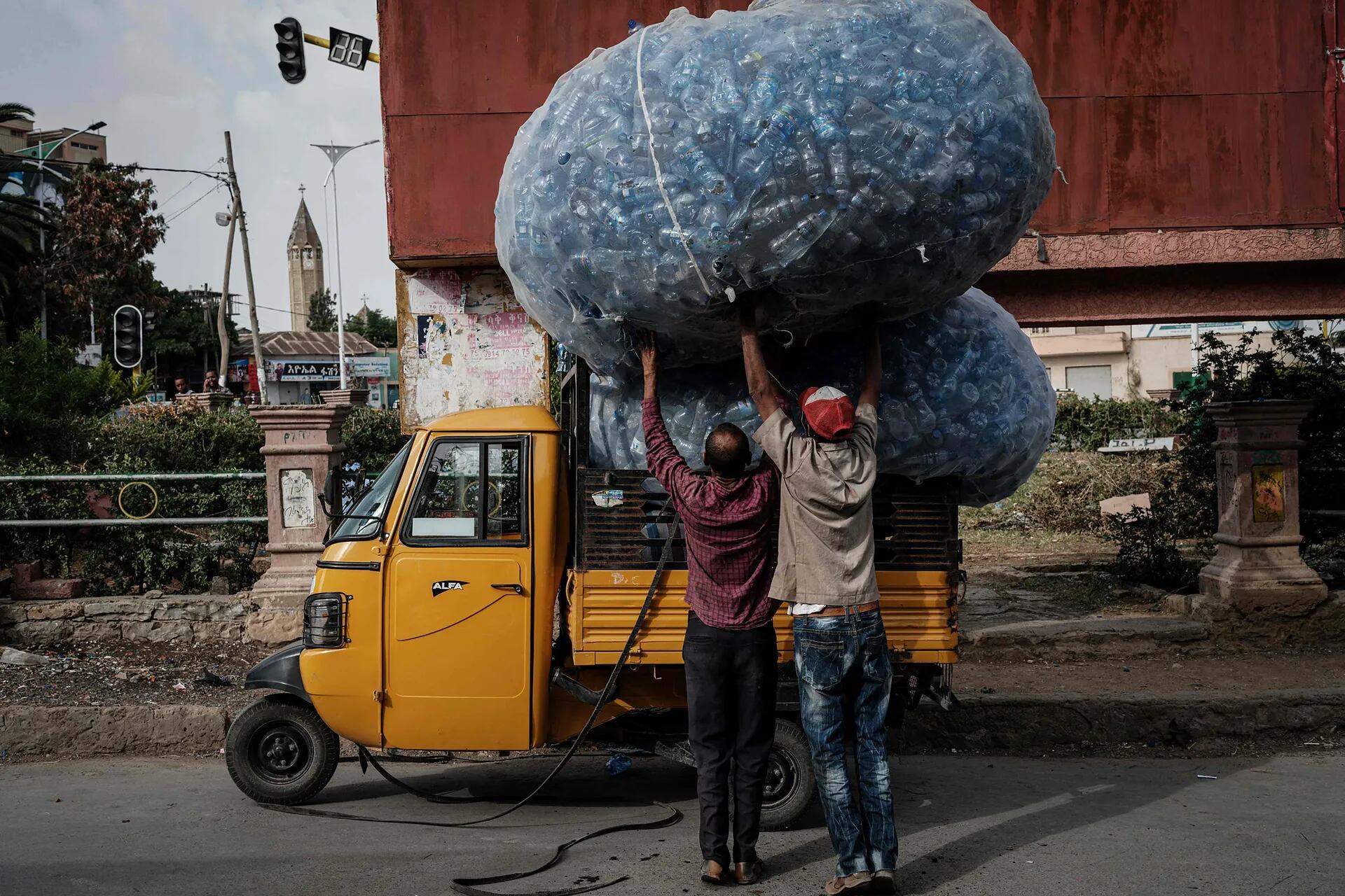 Dos hombres intentan empujar un saco lleno de botellas de plástico recolectadas para reciclarlas en un triciclo en Mekele, la capital de la región de Tigray, Etiopía.