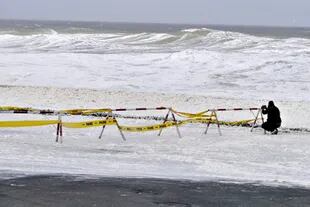 Un homma toma fotografías de la espuma del mar que cubre el paso martimo durante el paso a cyclin subtropical en Punta del Este, Uruguay.