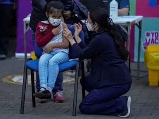 Un trabajador de la salud inocula a una niña contra el Covid-19 en la escuela Providencia en Santiago, Chile. (AP Foto/Esteban Felix)