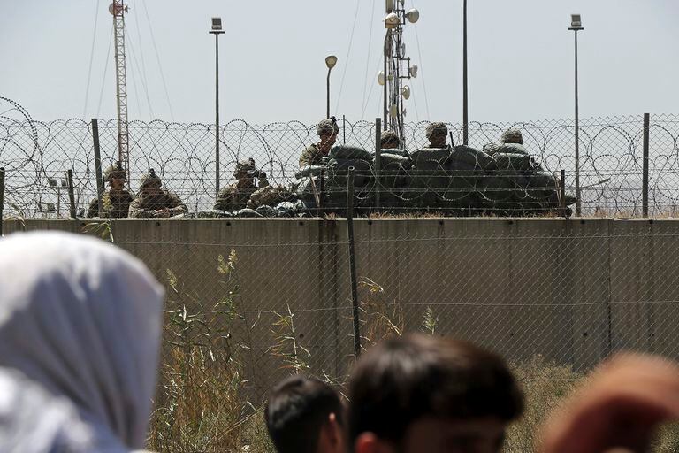 Soldados estadounidenses montan guardia dentro de los muros del aeropuerto mientras cientos de personas se reúnen cerca de un puesto de control de evacuación en el perímetro del aeropuerto internacional Hamid Karzai, en Kabul
