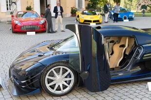 Las personas que miran un Koenigsegg One: 1 modelo 1 delante de un Aston Martin One-77 Coupe (2011), rojo, Ferrari LaFerrari (2015), amarillo, y un Bugatti Veyron EB 16.4 Coupe (2010), azul.