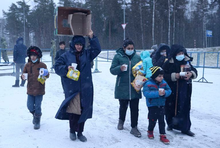 Migrantes llevan comida en un puesto de revisión del centro logístico "Bruzgi", en la frontera entre Bielorrusia y Polonia cerca de Grodno, el martes 30 de noviembre de 2021. (Oksana Manchuk/BelTA via AP)