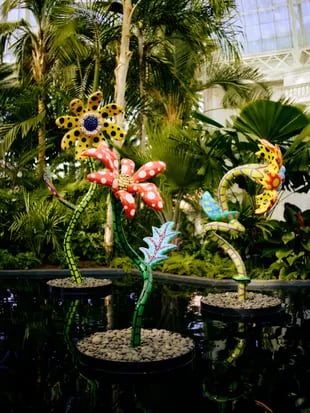 En un sector del botánico, se da una mezcla de enormes flores de acero pintadas de colores brillantes y palmeras naturales vivas