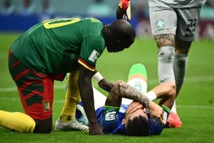 Alex Telles yace en el piso lesionado, lo asiste un futbolista de Camerún