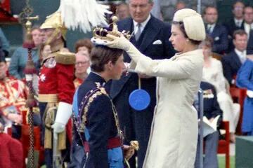 La reina Isabel II corona a su hijo Carlos, príncipe de Gales, durante su ceremonia de investidura el 1 de julio de 1969 en el Castillo de Caernafon en Gales, ante la mirada del secretario del Interior británico, James Callaghan