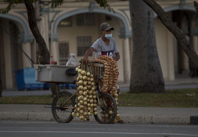 Un hombre con una mascarilla protectora vende ajos y cebollas en La Habana, Cuba, el jueves 30 de diciembre de 2021, en medio de la nueva pandemia de coronavirus.  (AP Foto/Ismael Francisco)