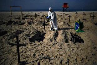 Un activista de la ONG Río de Paz, con un traje protector, cava tumbas en la playa de Copacabana para simbolizar a las víctimas del coronavirus durante una protesta contra la estrategia del gobierno 