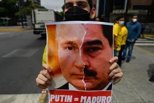 Un activista miembro del partido opositor Primero Justicia sostiene una pancarta con el rostro del presidente ruso Vladimir Putin y el presidente venezolano Nicolás Maduro durante una protesta contra la invasión rusa en Ucrania, en Caracas el 4 de marzo de 2022. 