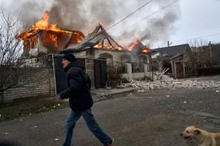 Un residente passa davanti a una casa in fiamme dopo un bombardamento russo a Kherson, in Ucraina, alla vigilia del Natale ortodosso, 6 gennaio 2023. (AP Photo/LIBKOS)
