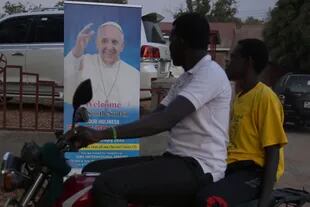 Un motociclista conduce con un pasajero junto a una pancarta que muestra el retrato del Papa Francisco mientras continúan los preparativos de su visita en Juba, el 30 de enero de 2023.