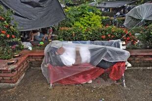 Un hombre se proteje de la lluvia con un plástico en un campamento improvisado en Mapastepec, Chiapas