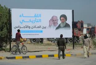 Los iraquíes caminan junto a un cartel que anuncia la próxima visita del Papa Francisco y una reunión con un venerado líder musulmán chiíta, el gran ayatolá Ali al-Sistani