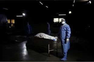 Un trabajador de la salud espera frente al cuerpo de un hombre que murió de covid-19, antes de su cremación en Nueva Delhi