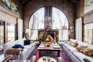 En el living de la casa grande, la gran arcada vidriada enmarca el hogar con un antiguo espejo pintado a mano en el centro.