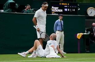 Drama moment at Wimbledon 2021: Roger Federer talking to Adrian Mannarino, lying on the floor after injury.
