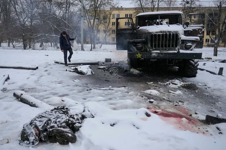 O corpo de um militar está coberto de neve enquanto um homem tira fotos de um veículo lançador de foguetes do exército russo destruído nos arredores de Kharkiv, Ucrânia, em 25 de fevereiro de 2022.