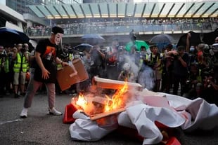 Un manifestante enmascarado prende fuego a una pancarta de celebración del 70 aniversario de China.