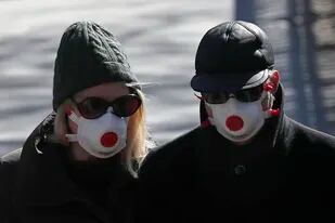 Dos personas con mascarilla atraviesan el Regents Park de Londres, 23 de marzo de 2020. El miércoles 23 de marzo de 2022 se cumplen dos años desde que se decretó la primera cuarentena por el coronavirus en Gran Bretaña. (AP Foto/Frank Augstein, Archivo)