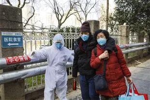 Un trabajador sanitario asiste a una pareja en las afueras de un hospital de Wuhan
