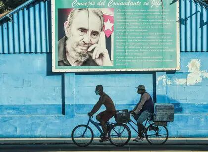 Men ride on their bicycles near a poster of Cuban late leader Fidel Castro in Havana, on July 12, 2021. - Thousands of Cubans took part in rare protests Sunday against the communist government, chanting, "Down with the dictatorship," as President Miguel Diaz-Canel called on his supporters to confront the demonstrators. The anti-government rallies started spontaneously in several cities as the country endures its worst economic crisis in 30 years, with chronic shortages of electricity and food. (Photo by YAMIL LAGE / AFP)